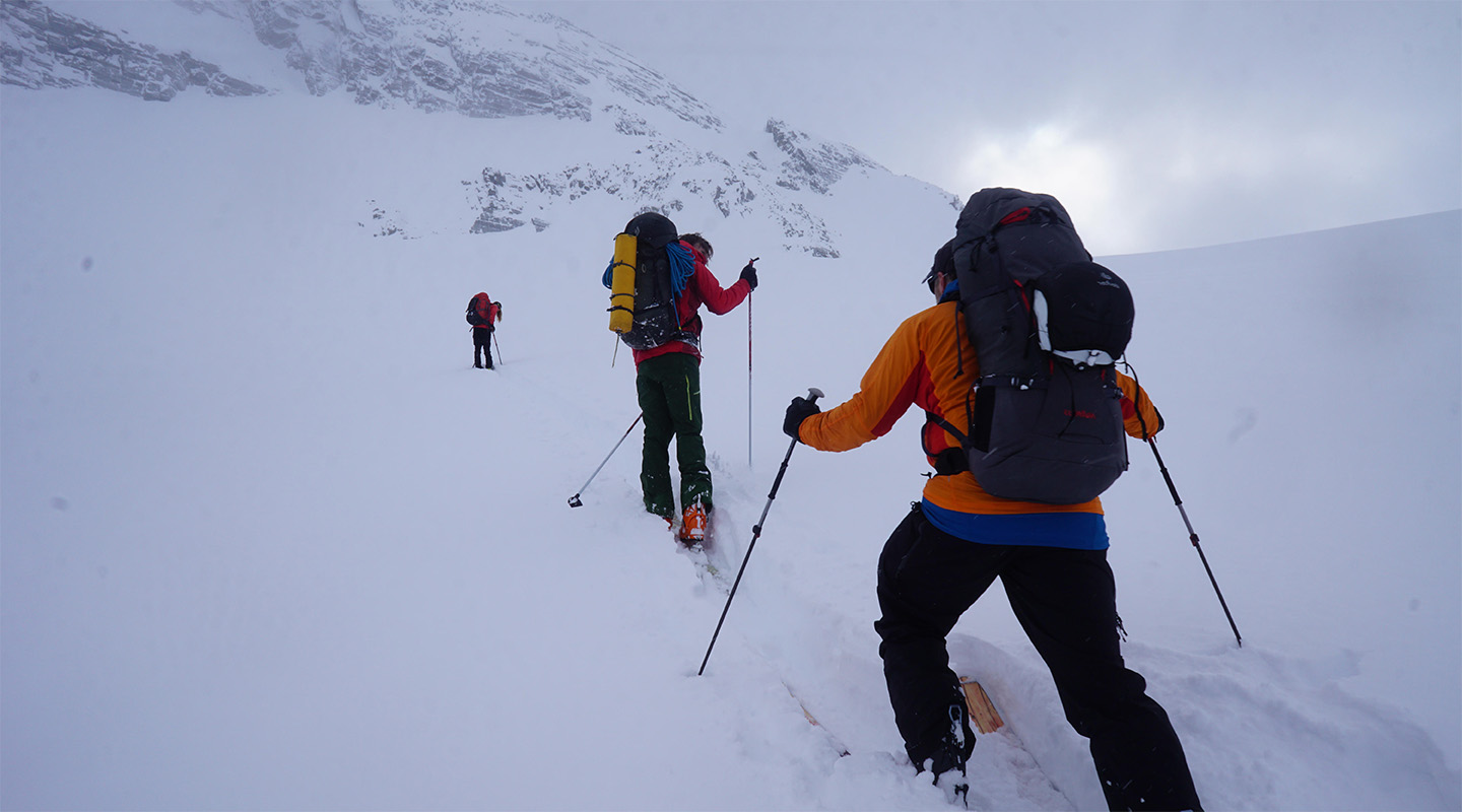 Three hikers climb a snow covered mountain.