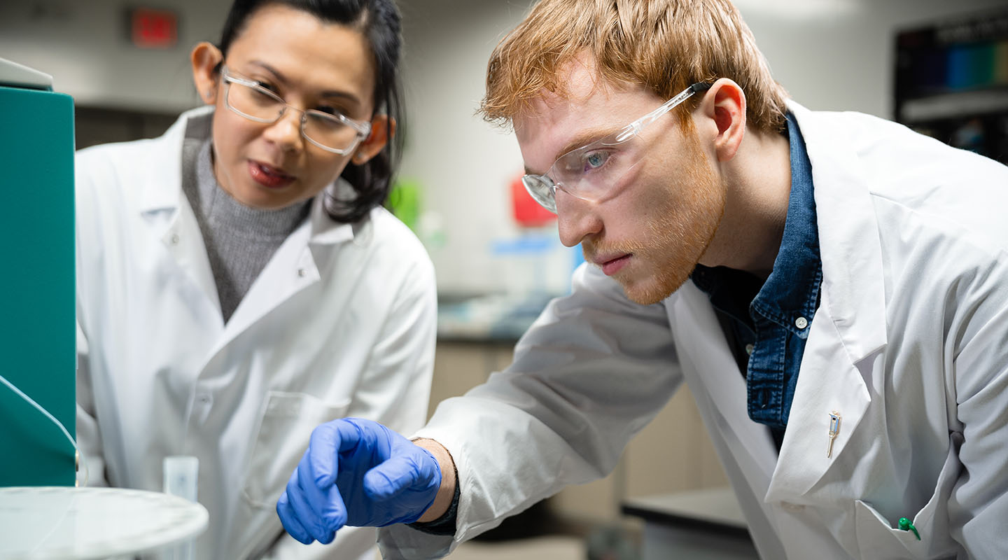 Two students in a chemistry lab looking at a piece of lab equipment.