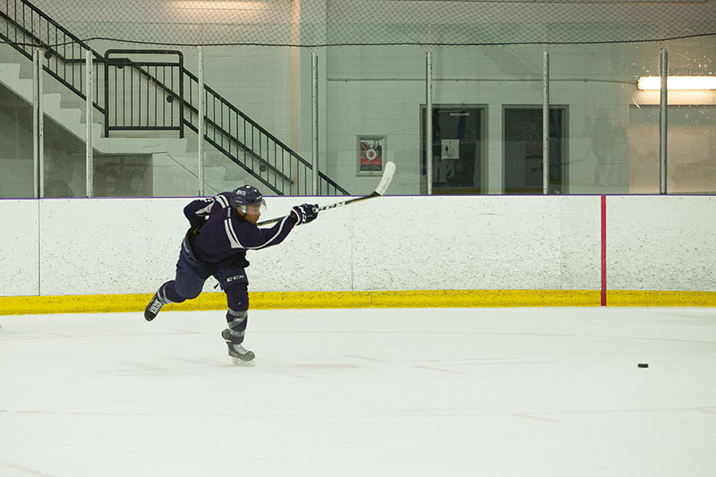 Mount Royal Cougars Men's Hockey player, Jamal Watson, takes aim to shoot a puck on the ice.