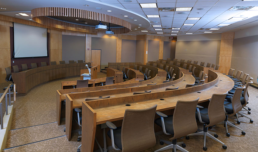 Rows of continuous, curved desks facing a central podium and desk for presenting.