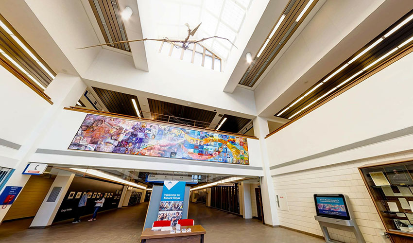 A bright, open space with a second floor looking down on it. The ceiling is is a triangular skylight and a pyersosaur skeleton is hung above the open area.