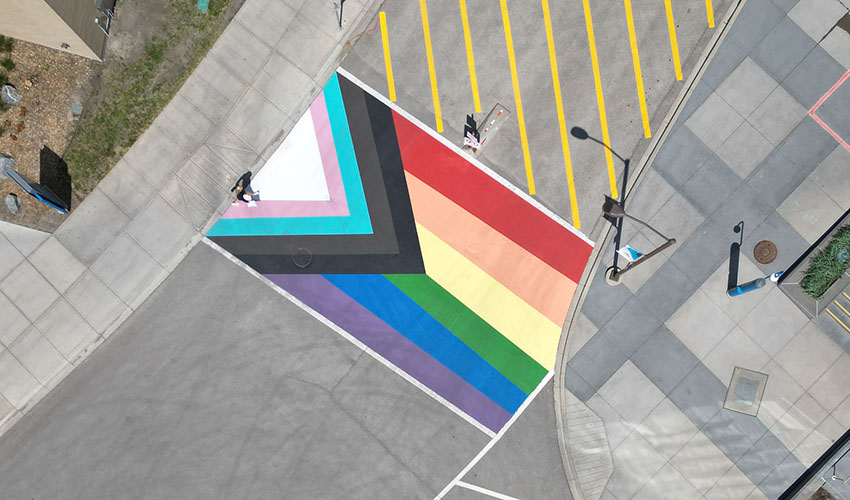 Aerial photo looking down on the progress pride flag painted on the road between the East Arts building and the Riddell Library and Learning Centre.