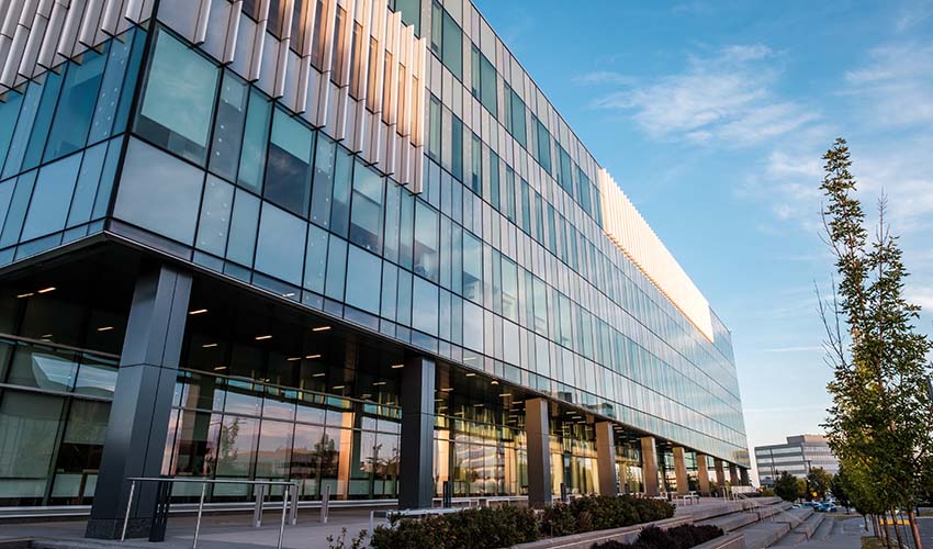 Photo of the Riddell Library and Learning Centre from the east side. It's a blue tinted glass building with rows of decorative metal details and concrete steps and garden beds.