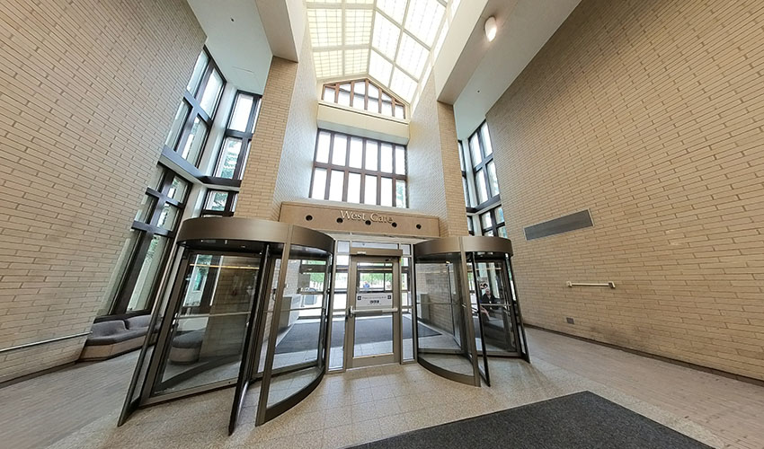 Low angle shot looking up at a triangular brick columned entrancway. There is a triangular skylight and columns of glass windows.