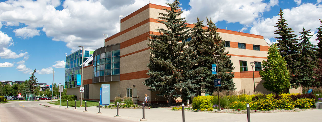 A red brick building with green and blue glass windows along a street on a sunny summer day.