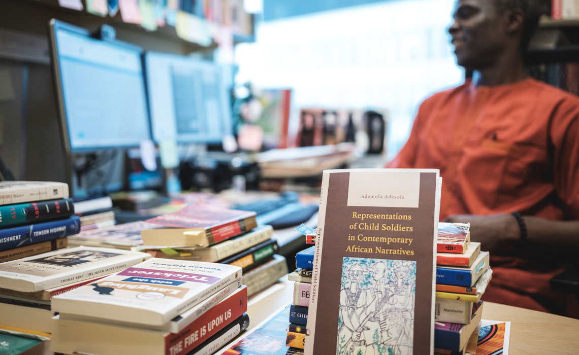 Ademola Adesola seated at his desk, focus on his book placed in front of him, surrounded by a calm study environment.