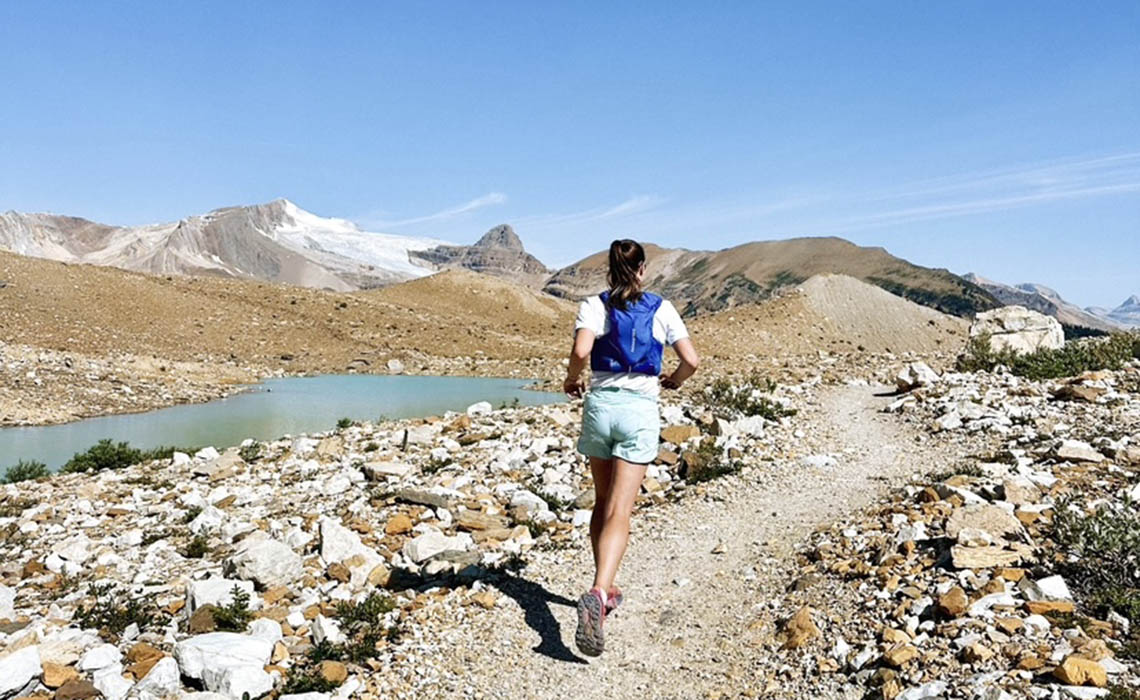 A woman runs on a winding mountain trail.