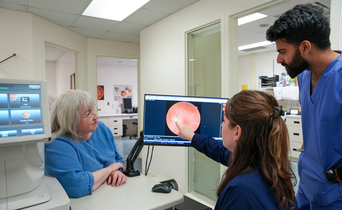 An optometrist and student optometrist focus on a computer screen, discussing patient information.