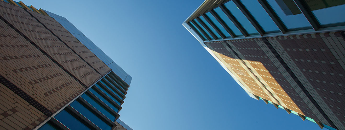 Photo looking directly up at a bright blue sky between two glass and patterned brick buildings.