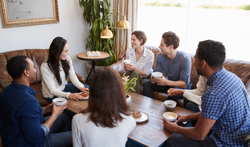 A group of people chatting and having coffee in a cozy, bright living room.