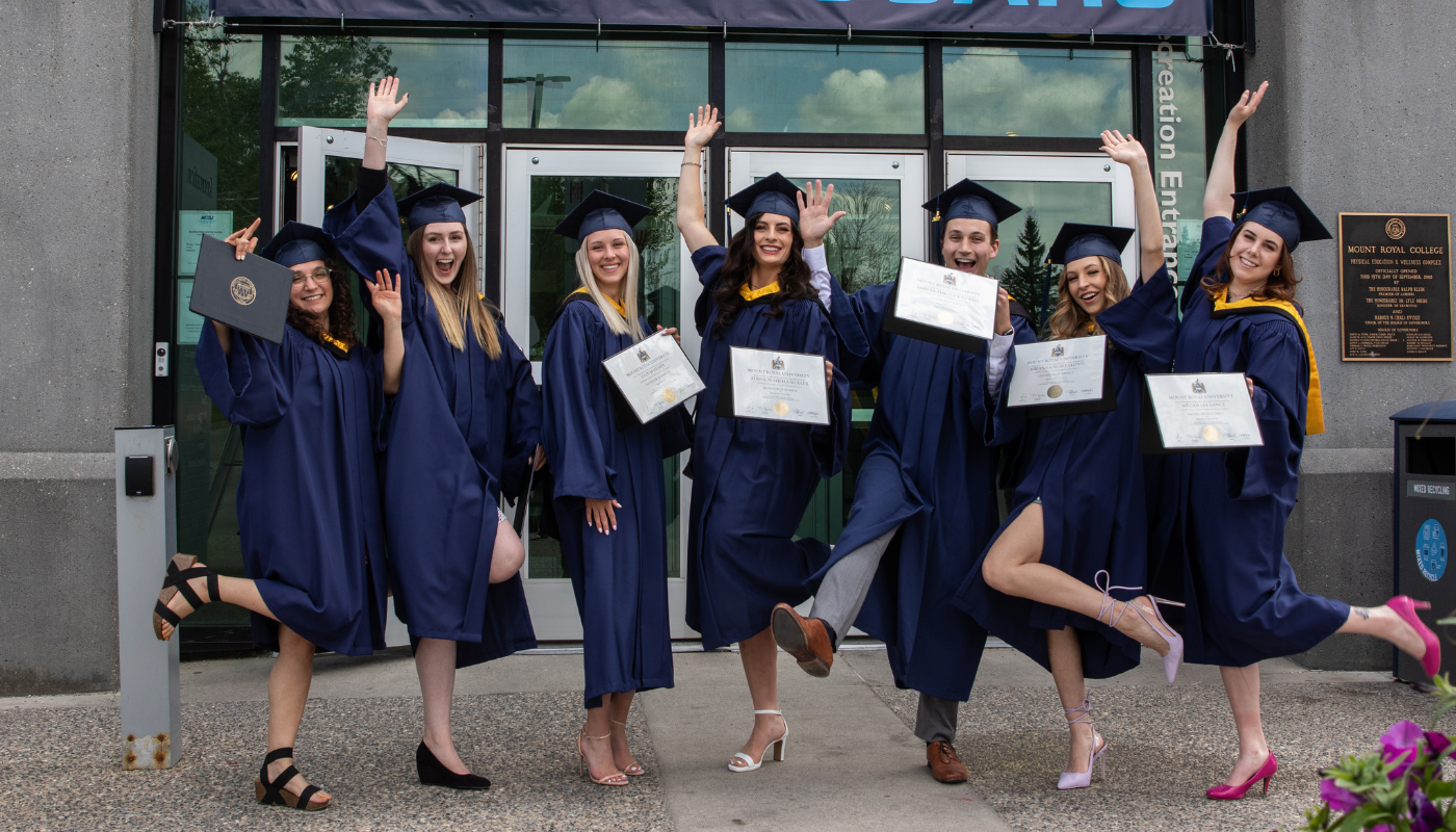 A group of new grads posing for a celebratory photo ourside the Recreation entrance of Mount Royal University.