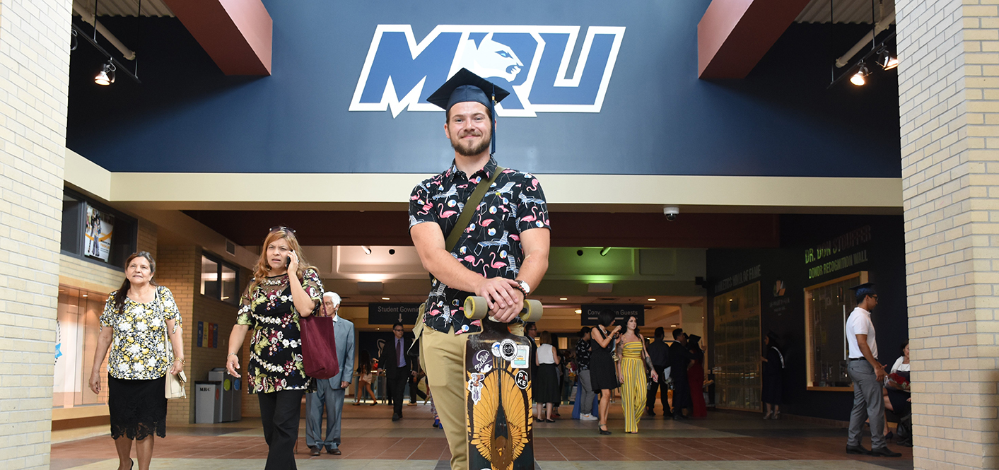 A grad posing in his cap and casual clothes in the Recreation entrance