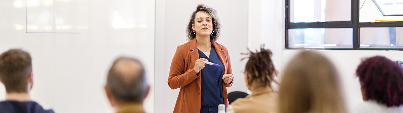 A woman at the front of a classroom instructing a group of professionals.