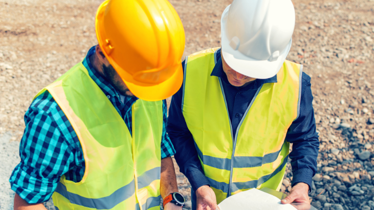 Two men in construction safety gear looking at a project plan
