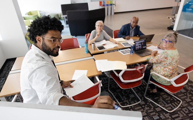 A young professional speaking to a group of professionals at a set of tables.
