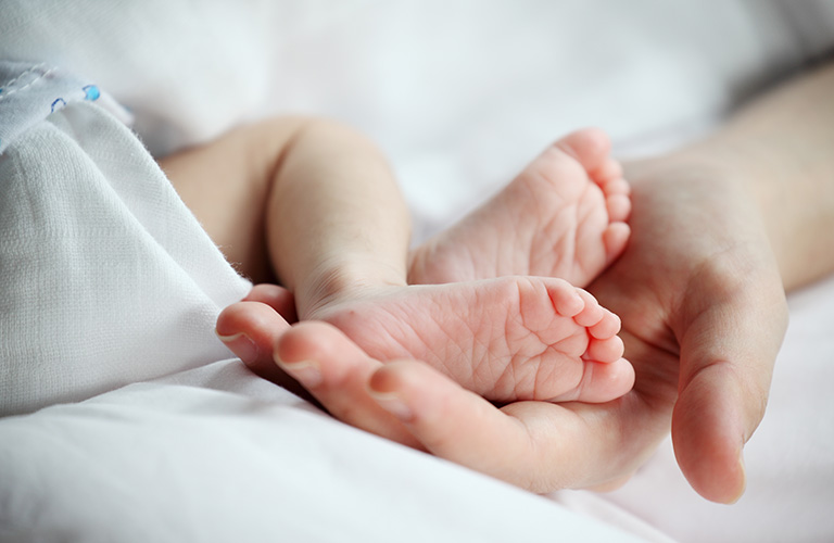 Close-up of a newborn baby’s feet resting in an adult hand.