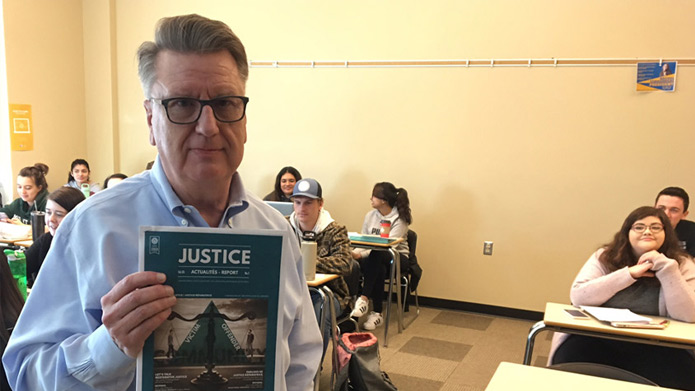Doug King, PhD, holding a copy of the Canadian Criminal Justice Association’s journal Justice Report in a classroom full of students