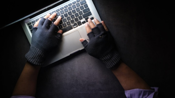 A pair of gloved hands types on a laptop.