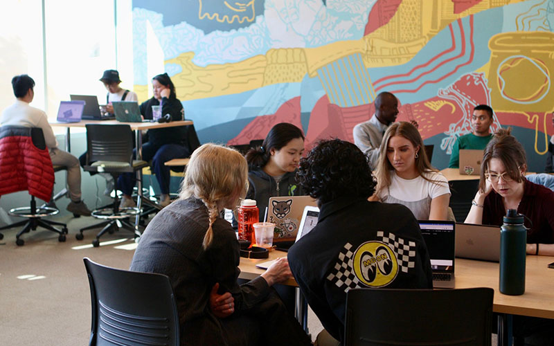 Many groups of people working at tables in the Slate Innovation Lab.