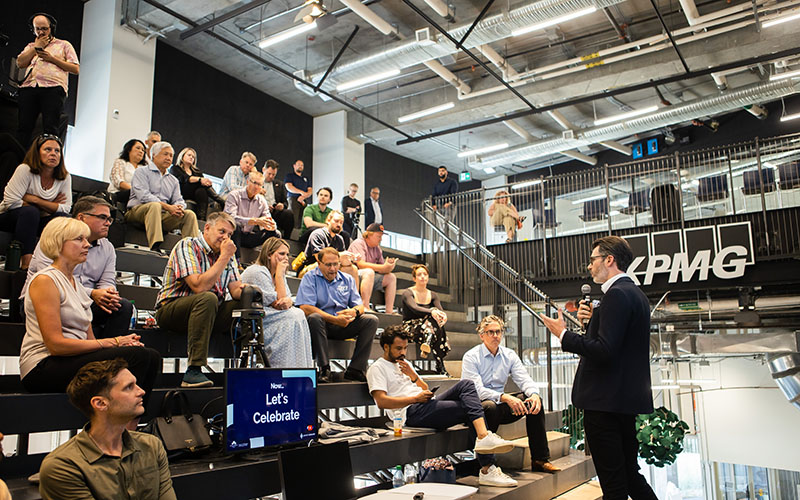 A person giving a talk to a group of professionals who are sitting on rows of steps.