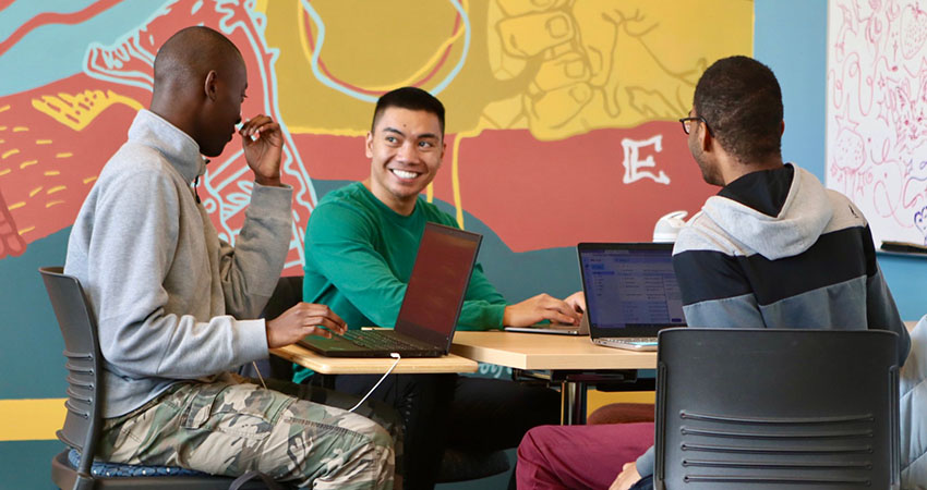 Three students at a table, actively working on laptops, in the Slate Innovation Lab.