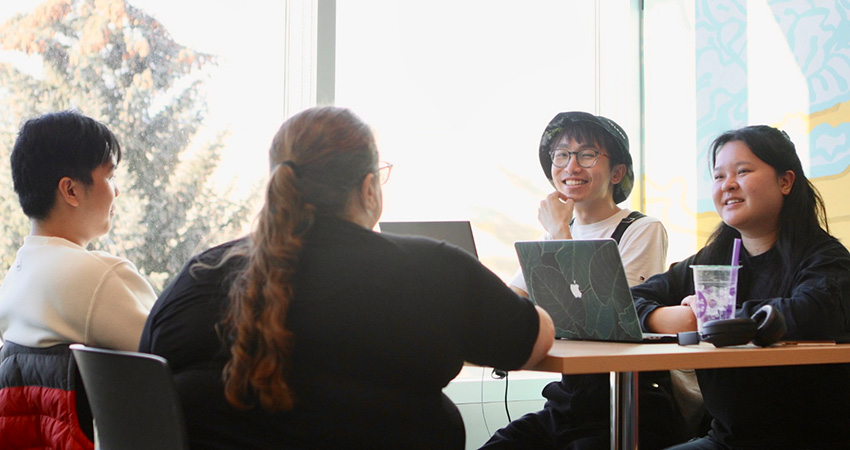 Four students by the window in the Slate Innovation Lab meeting to discuss a project.