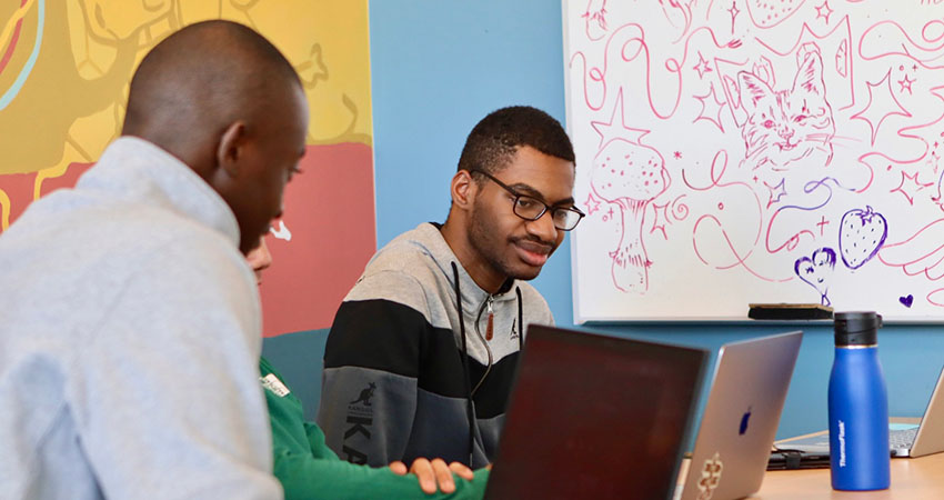 Three students in the Slate Innovation Lab working in front of a white board covered in whimsical doodles.