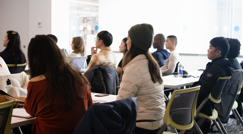 A group of people in a modern classroom listening to someone talk.