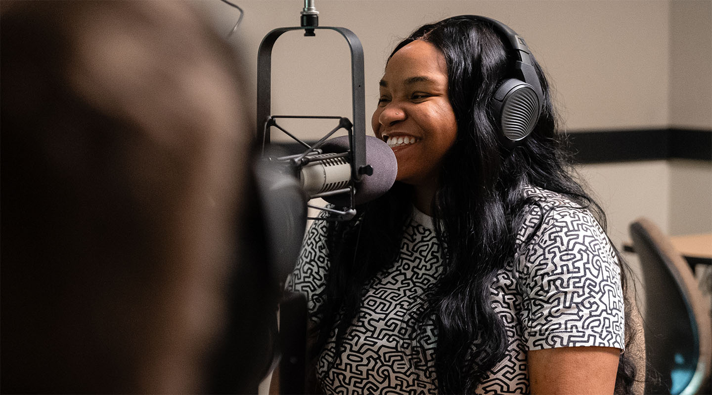 A woman sits smiling in front of a radio microphone.