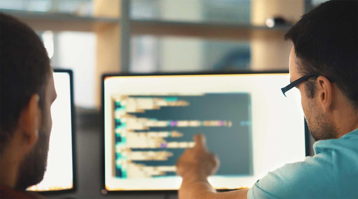 The backs of two people looking at a screen of code.