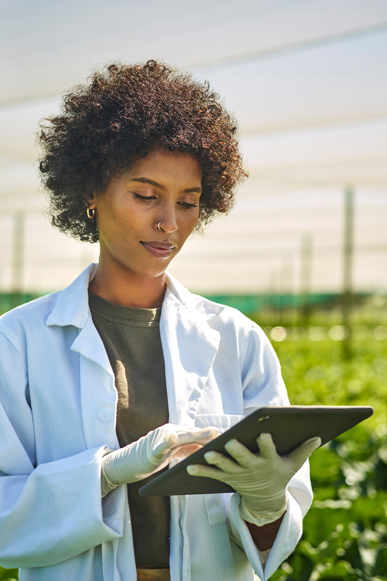 A woman in a lab coat is focused on using a tablet in a research setting.