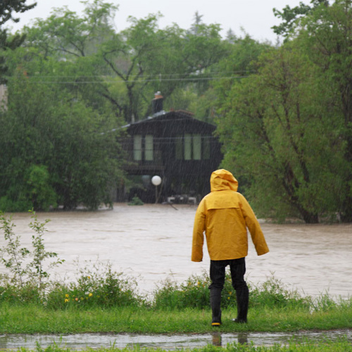 A person wearing a yellow raincoat observes a flooded property.